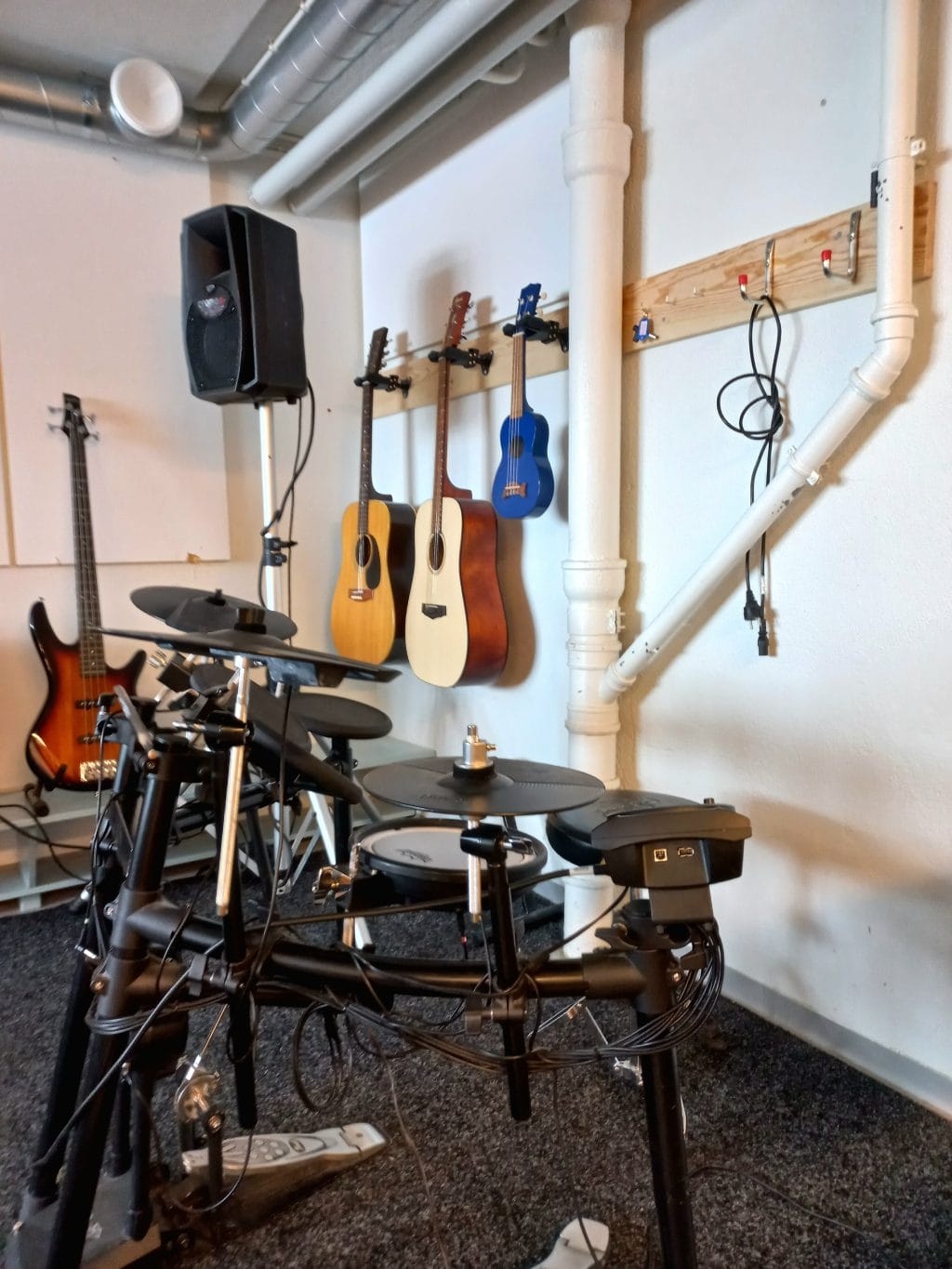 Kuva nuorisotoimen bänditilasta. Kuvassa näkyy sähkörummut, kitaroita ja ukulelejä