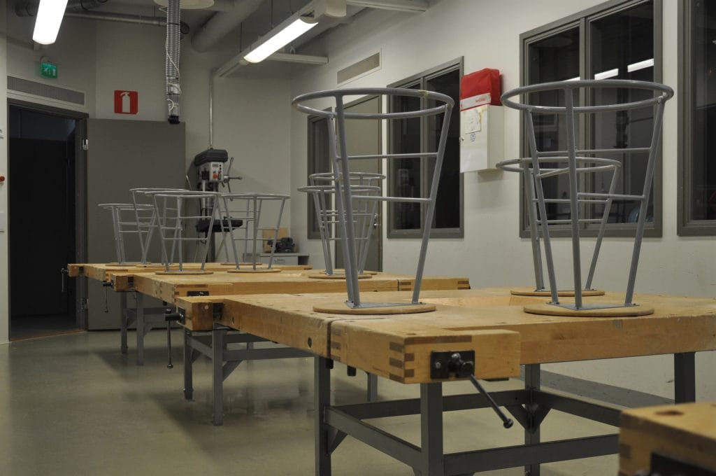 Valokuva Eskon koulun teknisen työn luokkahuoneesta. Oppilaiden istuimet on nostettu höyläpenkkien päälle.